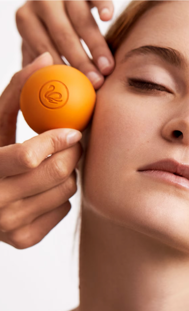 Person using Radiance C+ orange facial ball-roller on their face 